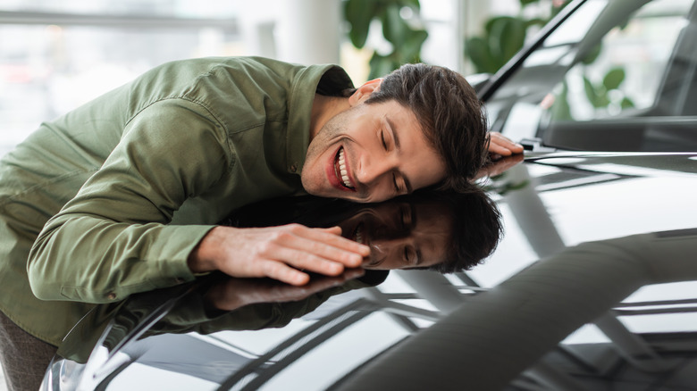 A man smiling while hugging the hood of a car.