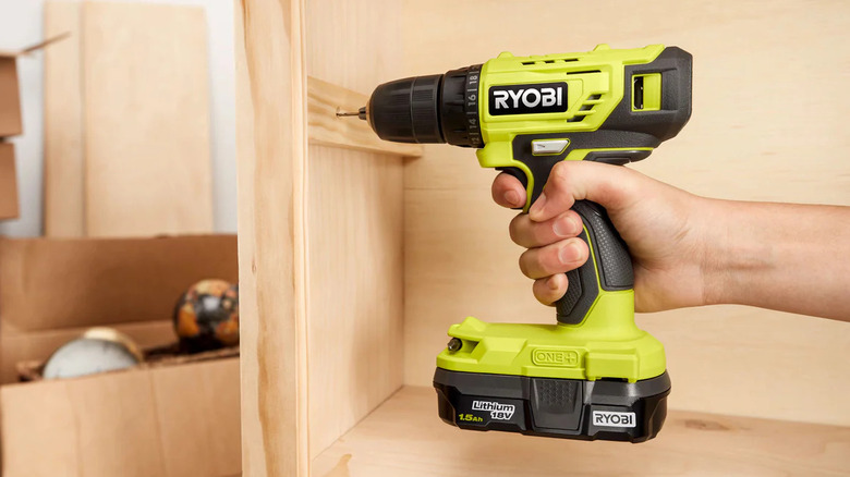 Green drill drilling into side of wooden cabinet