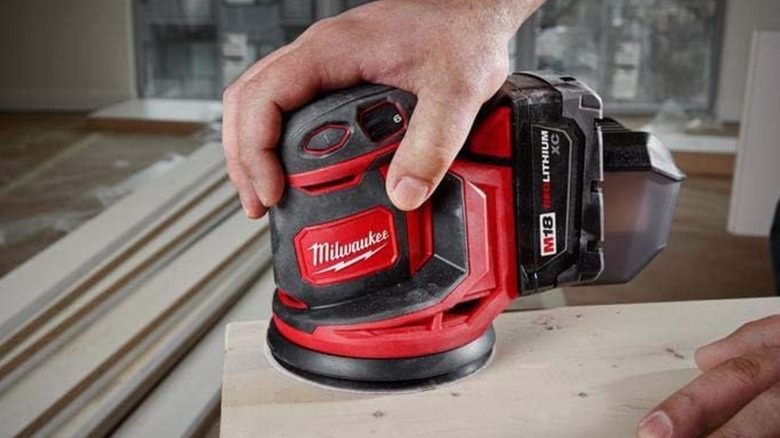 A Milwaukee orbit sander being held by a hand, used to sand wood