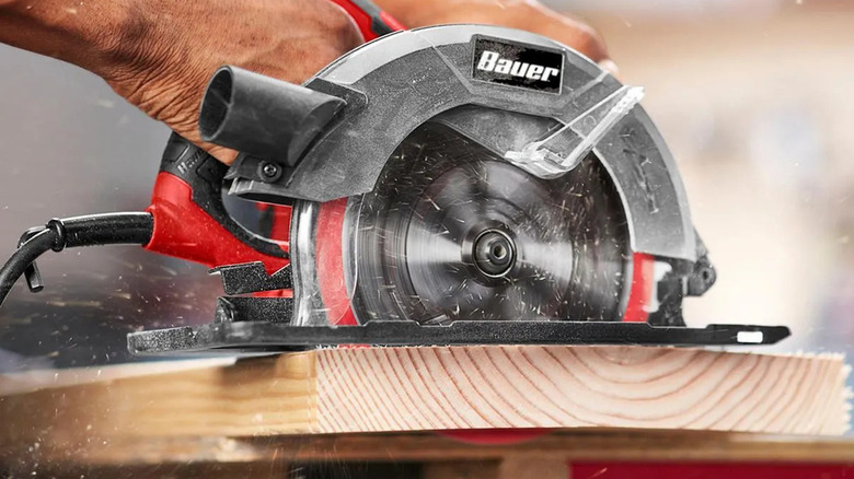The Bauer circular saw cutting a wooden plank, saw dust flying around it