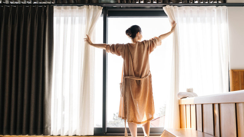 A woman opening her bedroom curtains