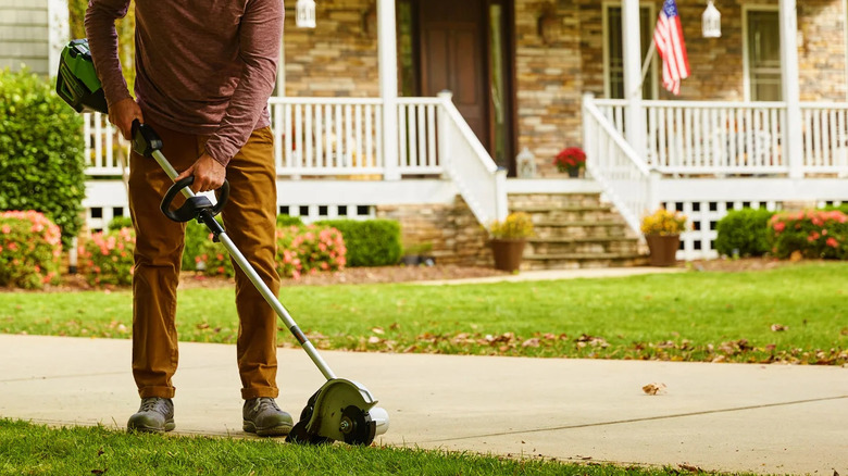 A person uses a Greenworks edger on the side of a walkway in a yard