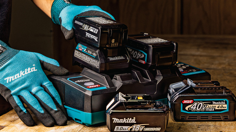 person with gloves holding Makita batteries