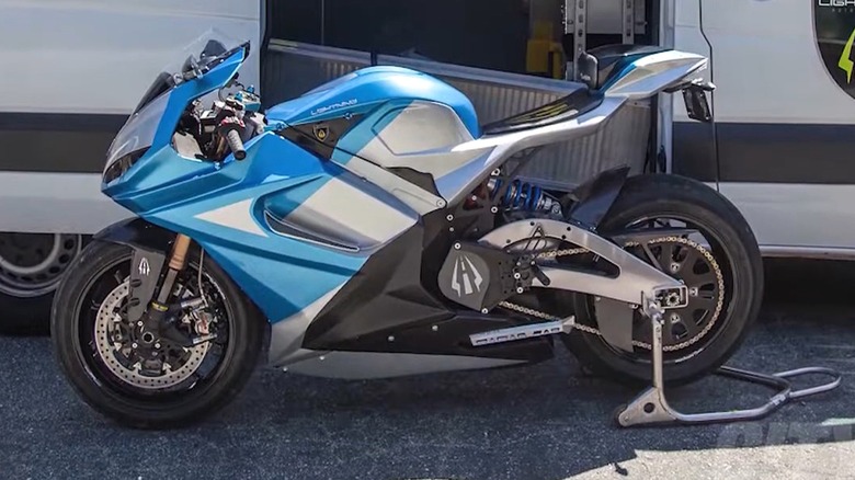 A blue Lightning LS-218 superbike in front of its branded Mercedes Sprinter support van loaded with charging equipment.