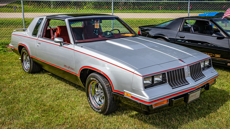 Front 3/4 view of silver and red 1984 Hurst/Olds parked at car show.