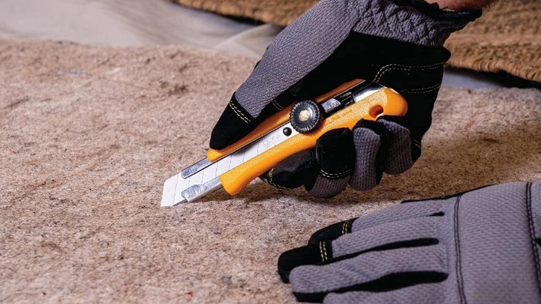 Person cutting carpet with OLFA 18mm Heavy-Duty Utility Knife