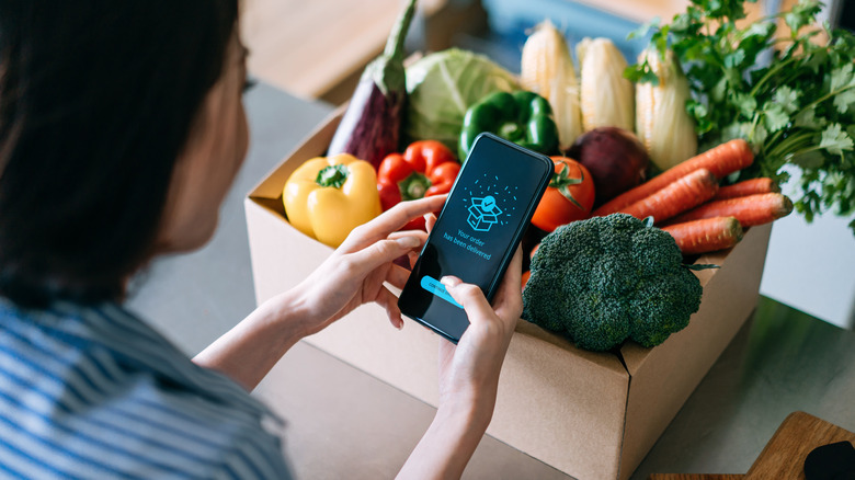 woman with an iPhone and a box of vegetables