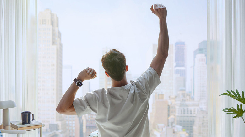 A person wearing a Samsung Galaxy and stretching on bed looking at city skyline through a large window.
