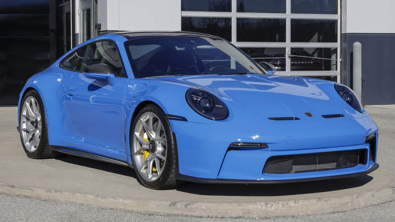A blue Porsche 911 GT3 Touring parked in front of a dealership.