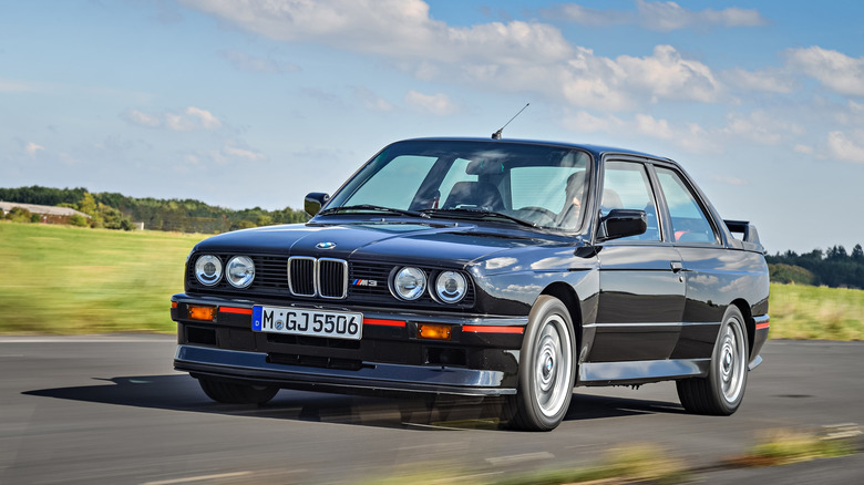 BMW E30 M3 driving at speed on track, front-left 3/4 view