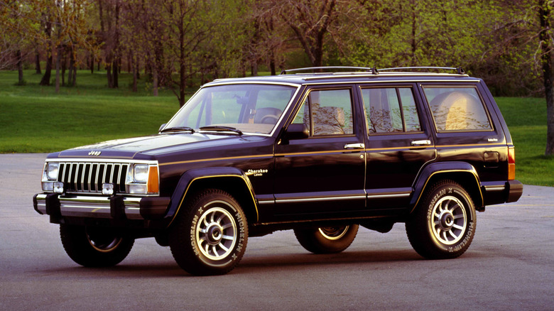 1985 Jeep Cherokee XJ parked in lot in front of woods, front-left 3/4 view