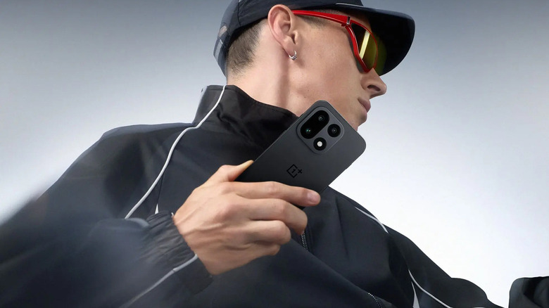 Promotional image of a person dressed in a black tracksuit holding a black OnePlus 15