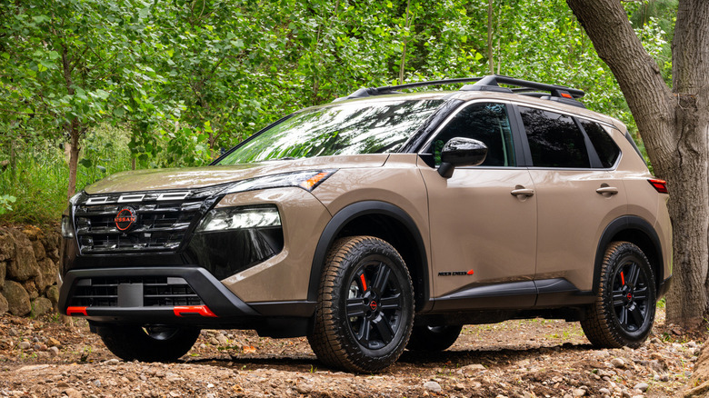 Front 3/4 view of 2027 Nissan Rogue parked next to tree in of-road setting
