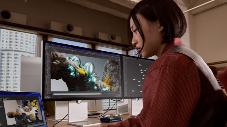 Woman looking at laptop next to Apple Studio Display