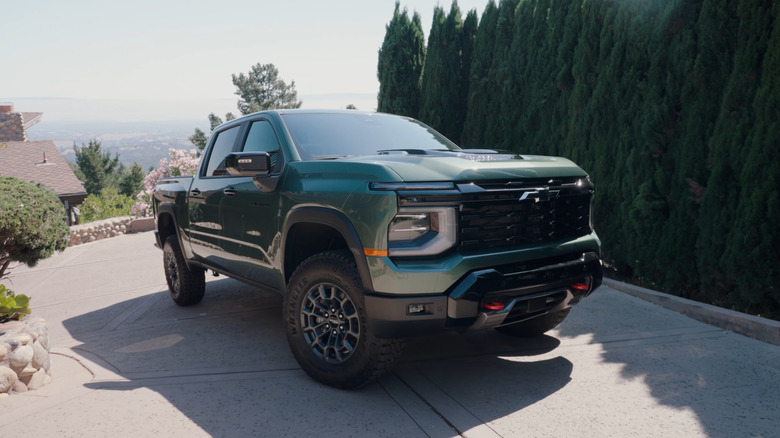 2027 Chevrolet Silverado Trail Boss in green on a hilly driveway, front 3/4 view