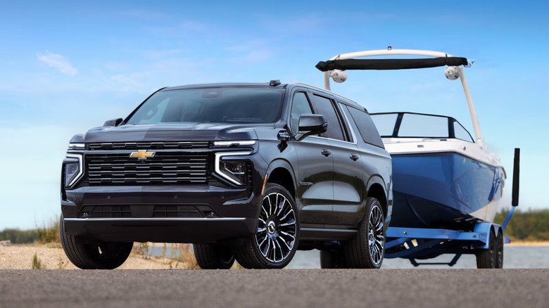 2027 Chevrolet Suburban towing boat on trailer, front-left 3/4 view, low-angle shot