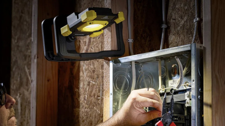 A man using the BRAUN LED Rechargeable Heavy Duty Clamp Light while doing electrical work in a dark space