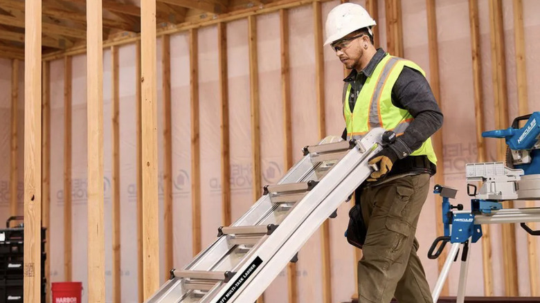A workman moving the Franklin 22-ft ladder with wheels in a construction space