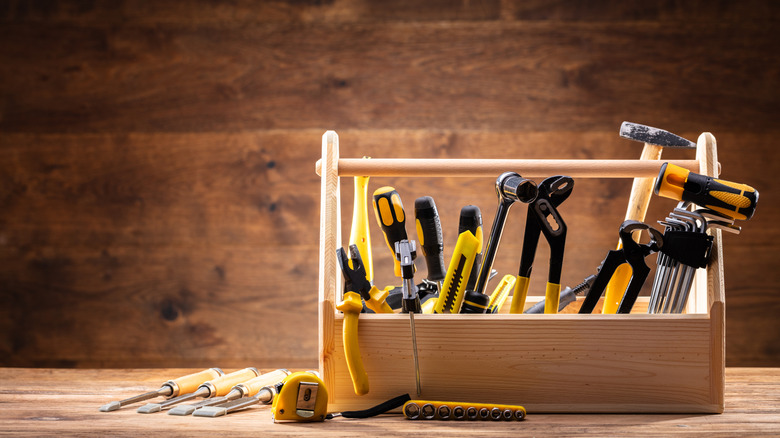 A set of yellow tools in a wooden tool box sitting against a wooden surface