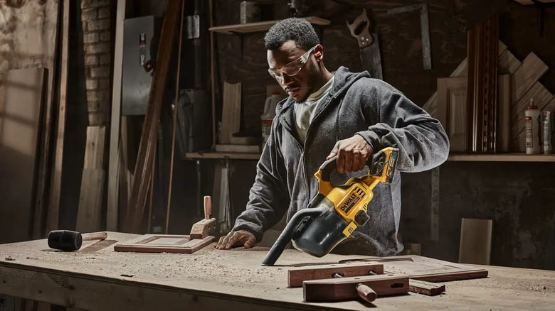 A man using a handheld DeWalt Vacuum Cleaner to clean wood filings