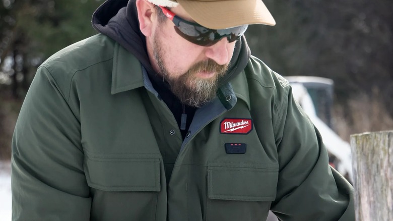 A man wearing a Milwaukee jacket working in a snowy yard.