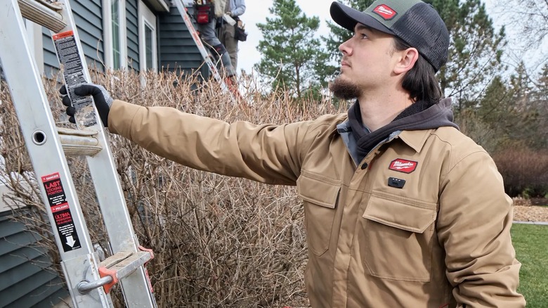 A man wearing a Milwaukee heated jacket holding up a ladder.