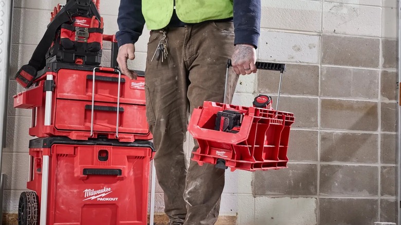A person carrying a Milwaukee Packout Compact Crate by its handle