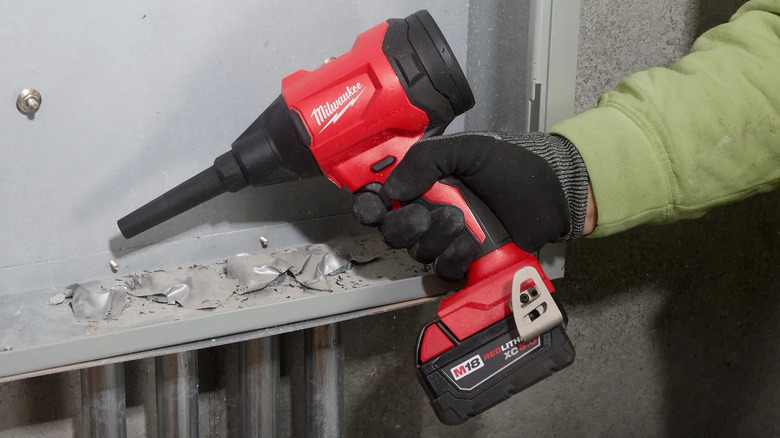 person blowing debris from electrical junction box with tool