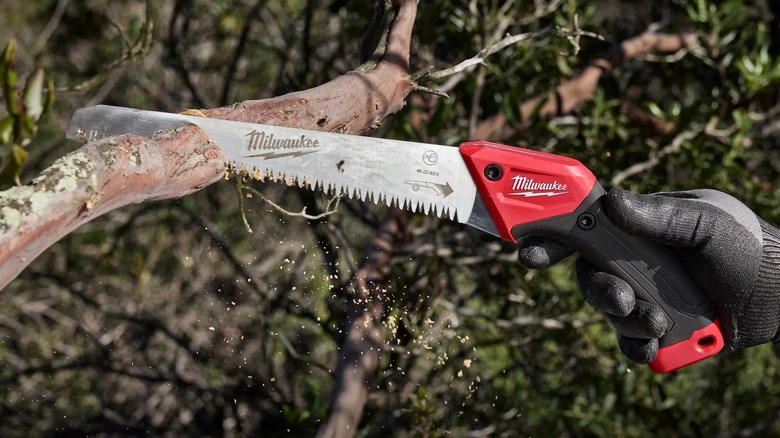 A person using a Milwaukee saw on a branch.