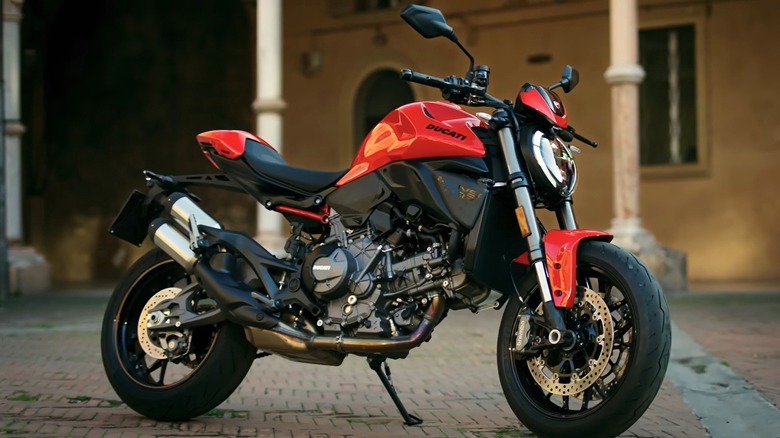A Ducati Monster+ in red and black is parked in front of a building.