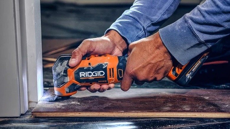 A Ridgid oscillating multi-tool being used to saw the bottom of a door frame.
