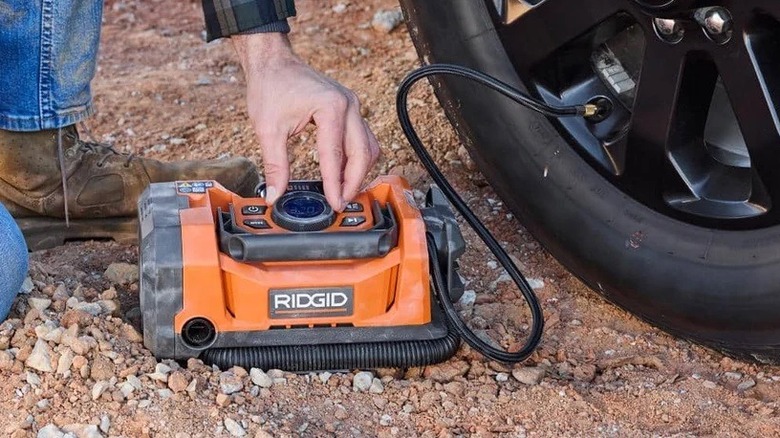 Ridgid cordless dual-function inflator inflating a tire on rough ground.