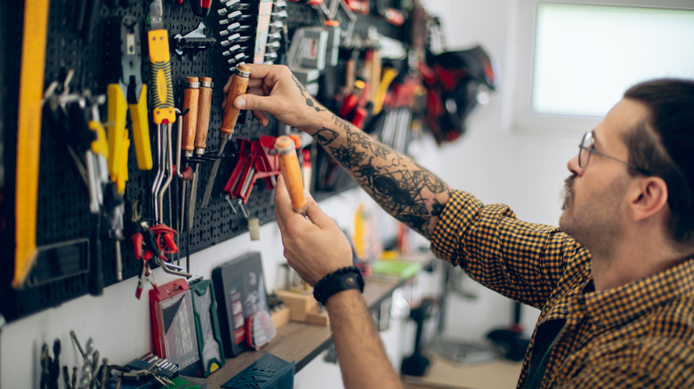 A man in a yellow and black plaid shirt putting away tools on a peg board
