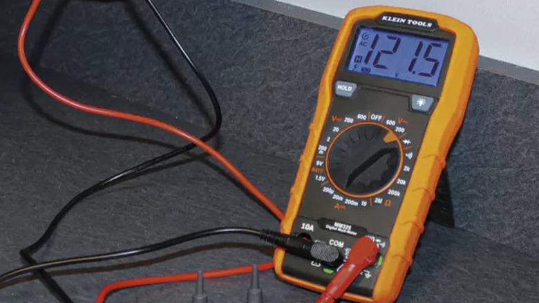 An orange Klein Tools multimeter propped against a wall and in use