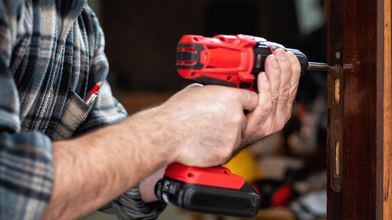A man using a red electric drill to install a screw in a door frame