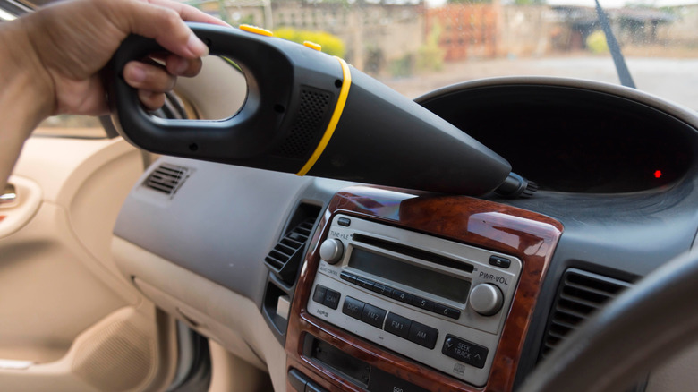 Handheld vacuum being used on a dashboard