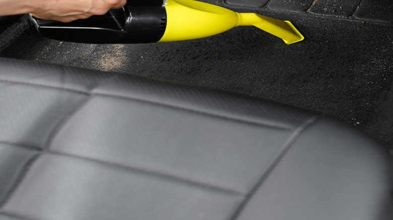A handheld vacuum being used on a car's carpets