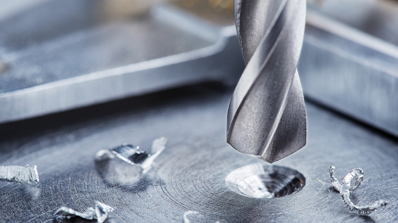 A close-up of a drill bit drilling a hole in a piece of metal, metal shavings around it