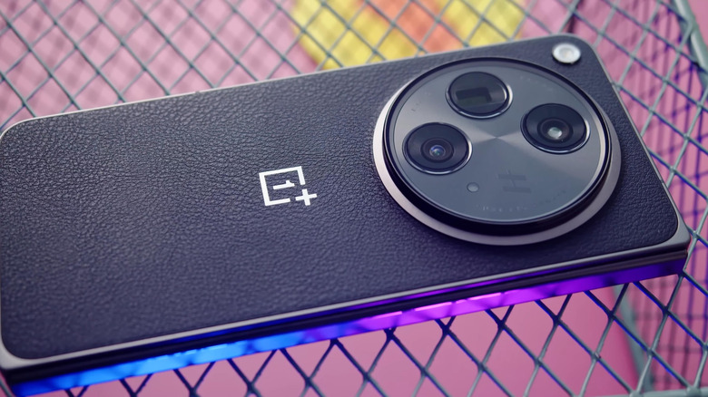 Closeup of OnePlus 15 smartphone resting on wired surface.