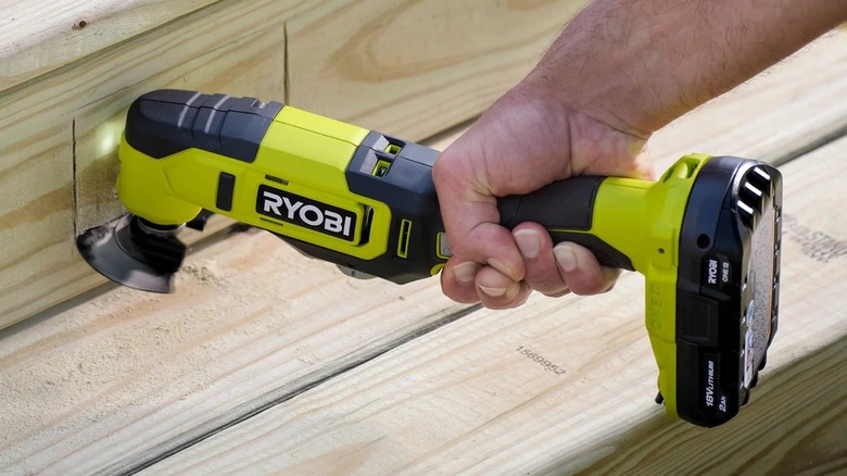 A person using a Ryobi multitool on wood.