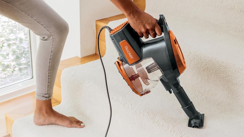 Person using Shark Rocket vacuum cleaner on carpeted stairs