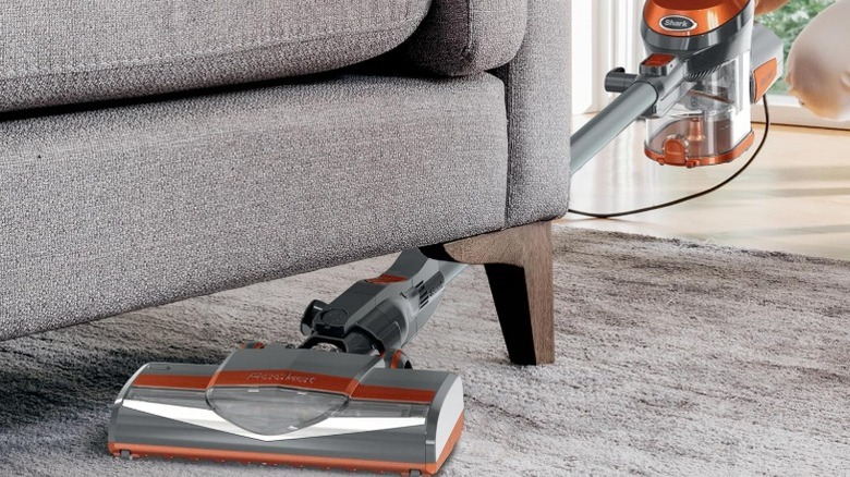 Person using Shark Rocket Corded Stick Vacuum Cleaner to vacuum under sofa