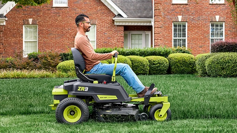 Worker mowing lawn with Ryobi zero-turn mower