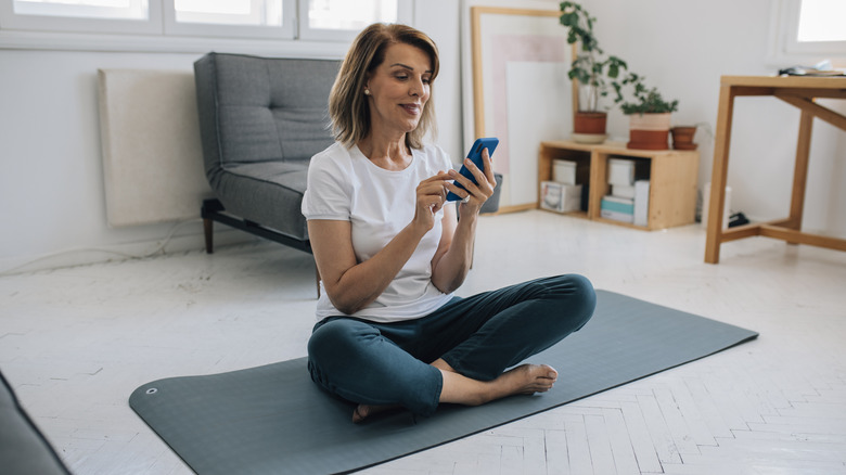 woman on yoga mat holding phone