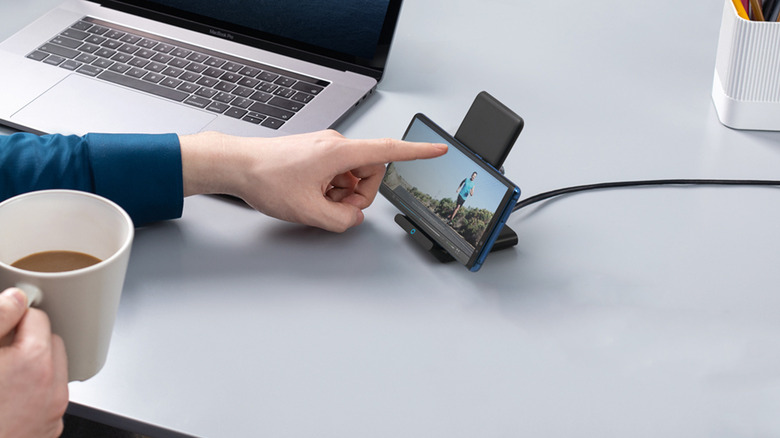 Person using a phone while it's charging on a wireless charging stand.