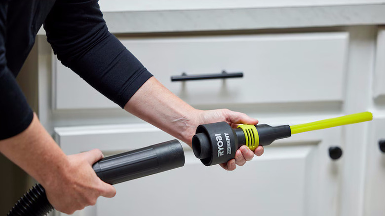 A person places a green and black micro crevice vacuum attachment on a hose.