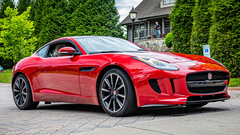 Jaguar F-Type coupé parked in front of trees and a building.