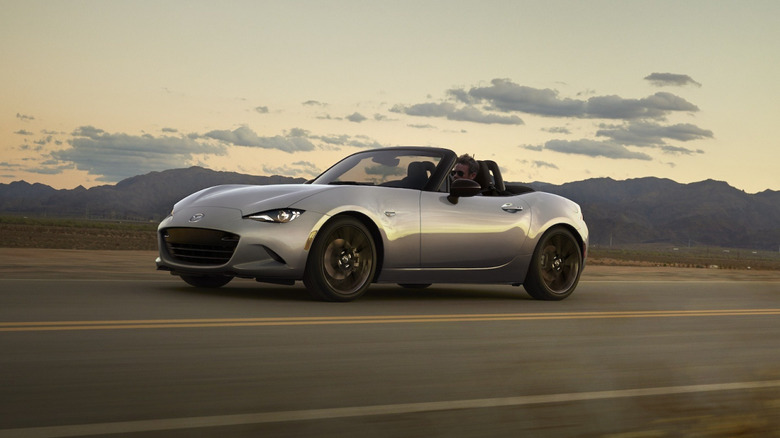 A Mazda Miata drives along the highway at sunset with the top down.