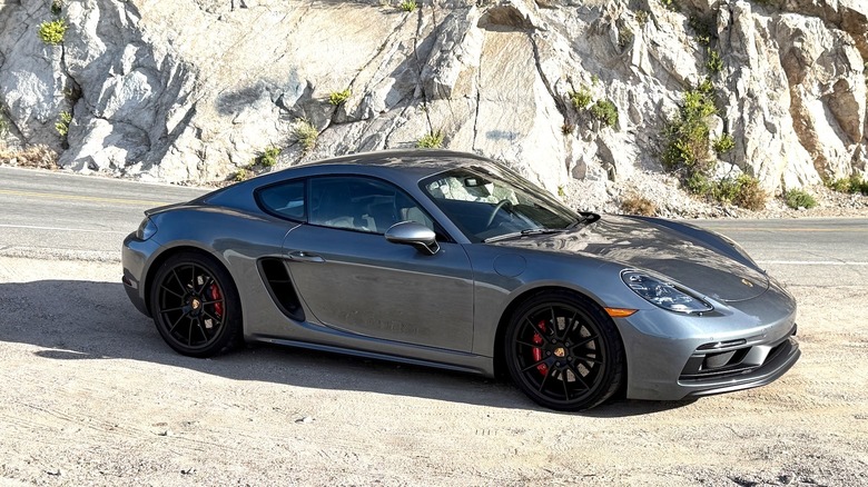 Porsche Cayman GTS 4.0 parked on the side of the road in front of a rocky mountainside.