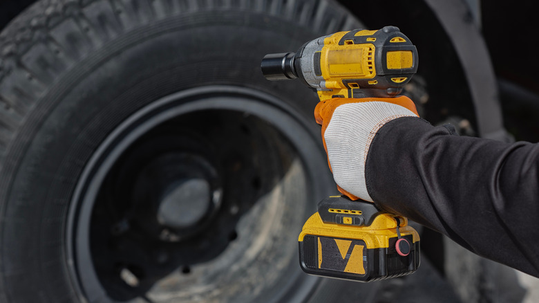 A yellow impact wrench pointed at a large tire.